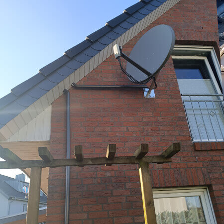 Eine Sattelitensch&uuml;ssel an einer Fassade und vom Dach heruntergef&uuml;hrtes Elektroinstallationsrohr